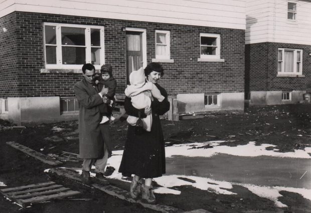 Photo noir et blanc d’une famille marchant sur des planches pour éviter la boue.