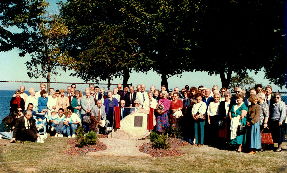 Photo couleur d’un large groupe de personnes près d’une pierre sur laquelle est fixée une plaque.