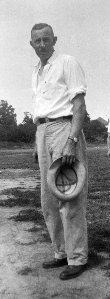 Photo noir et blanc d’un homme les manches relevées et tenant un chapeau.