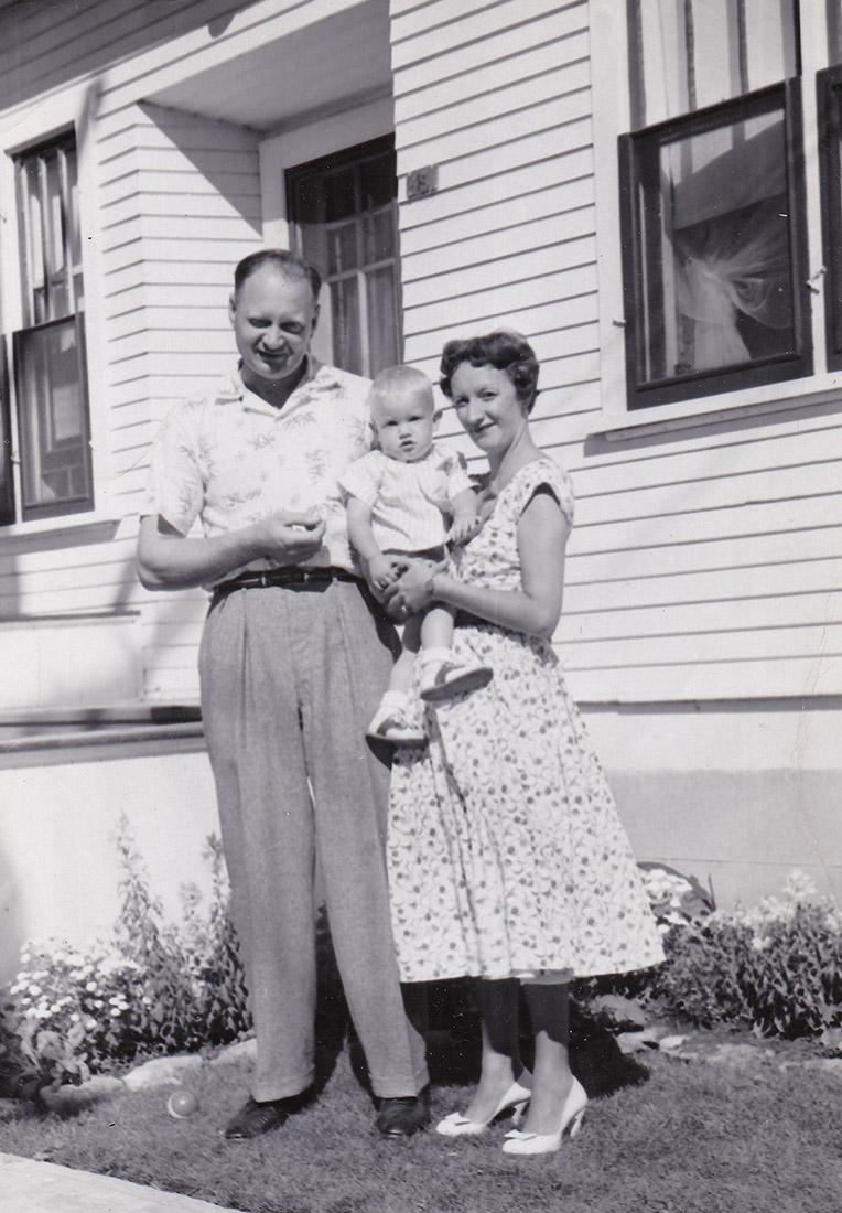 Photo noir et blanc d’un homme, d’une femme et d’un petit enfant devant une maison.