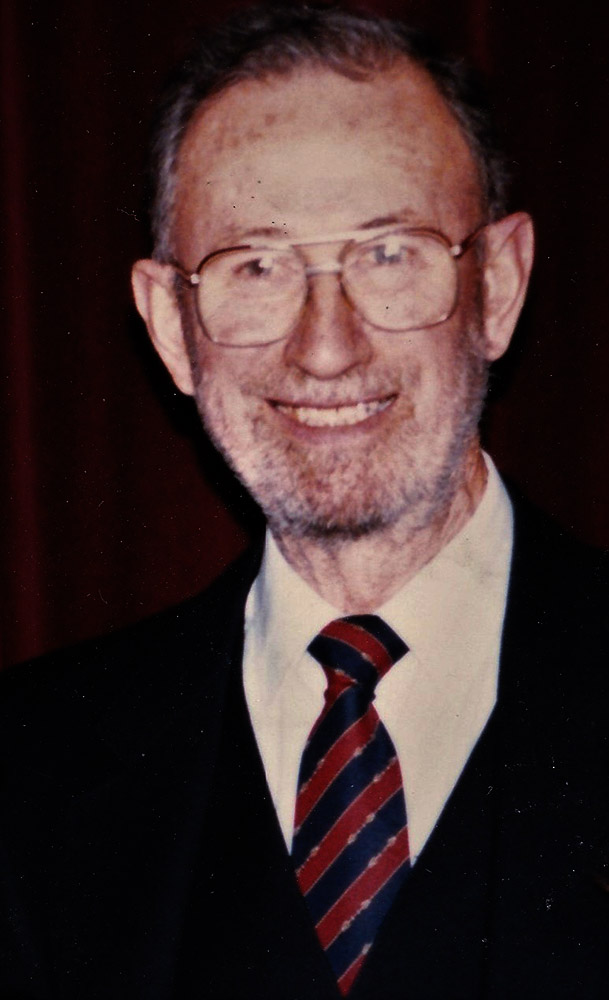 Photo couleur d’un homme en costume de ville et portant des lunettes.