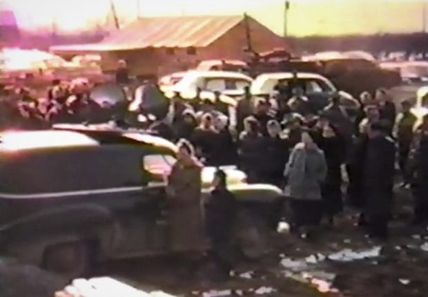 Ancienne photo couleur d’un groupe de personnes debout près de plusieurs voitures.