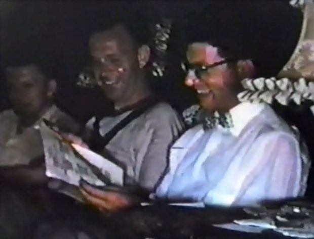 Ancienne photo couleur de deux hommes lisant des documents et souriant.