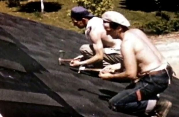 Photo couleur de deux hommes posant des bardeaux, l’un en casquette bleue et l’autre en casquette blanche, tous deux torse nu.