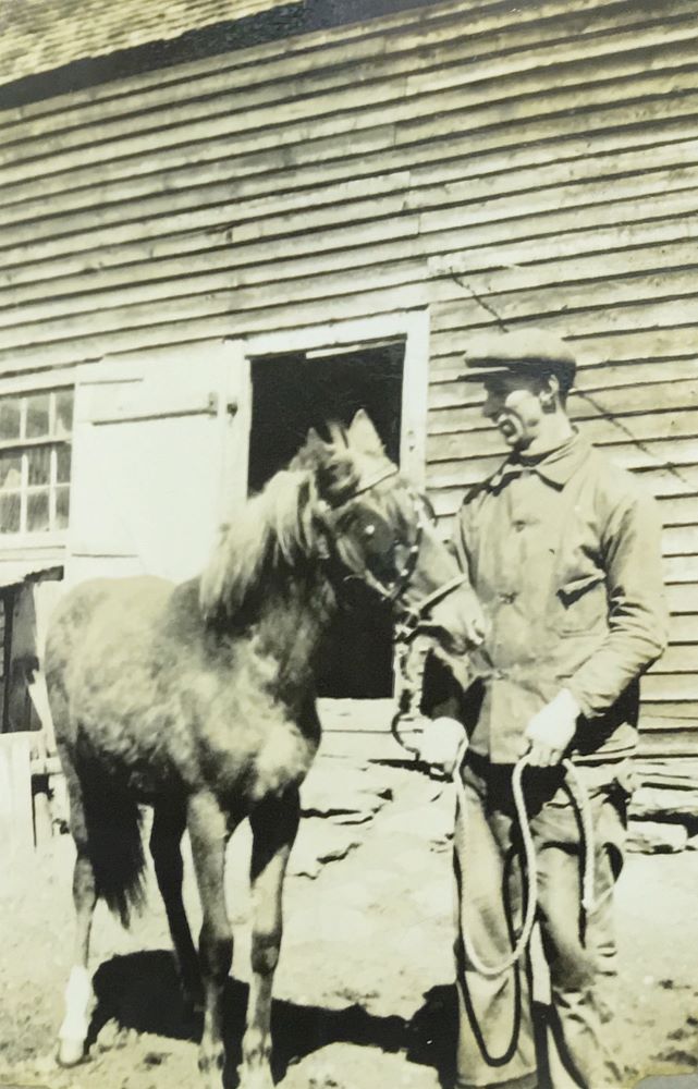 Photographie en noir et blanc d’un jeune homme posant à côté d’un cheval.