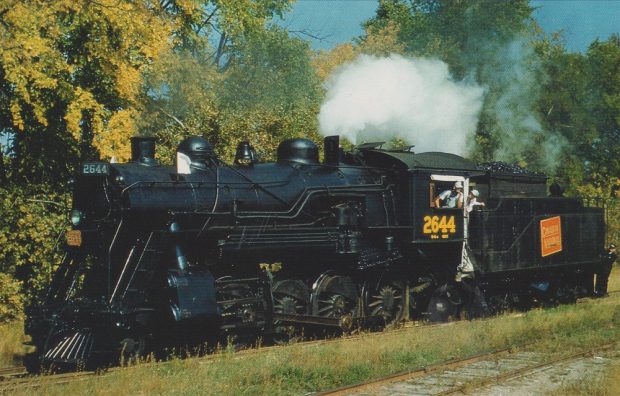 Image en couleur d’une locomotive à vapeur, avec des arbres à l’arrière-plan