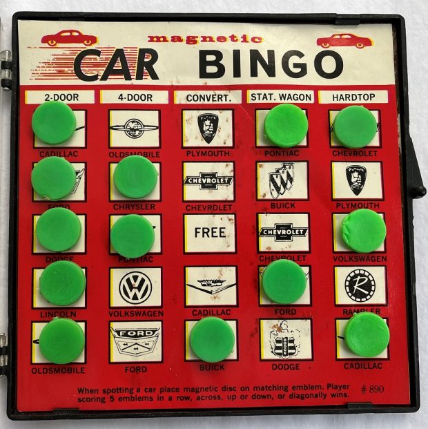 Photo couleur d’un plateau de jeu de plastique avec des jetons verts et une feuille qui montre des logos des fabricants variés de voiture 