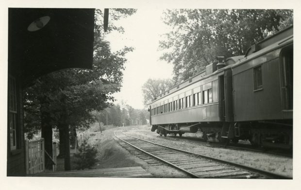 Image en noir et blanc d’un train avec chemin de fer à l’avant-plan et des arbres à l’arrière-plan