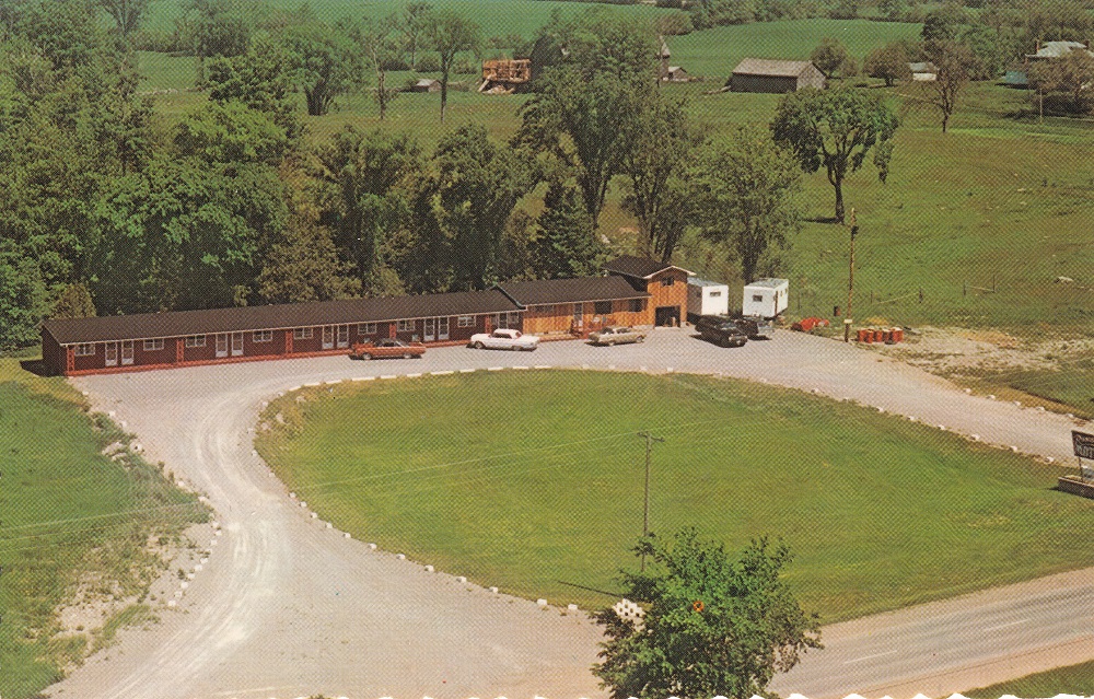 Photo aérienne en couleur d‘un long bâtiment, de voitures anciennes, d’une pelouse et de l’autoroute