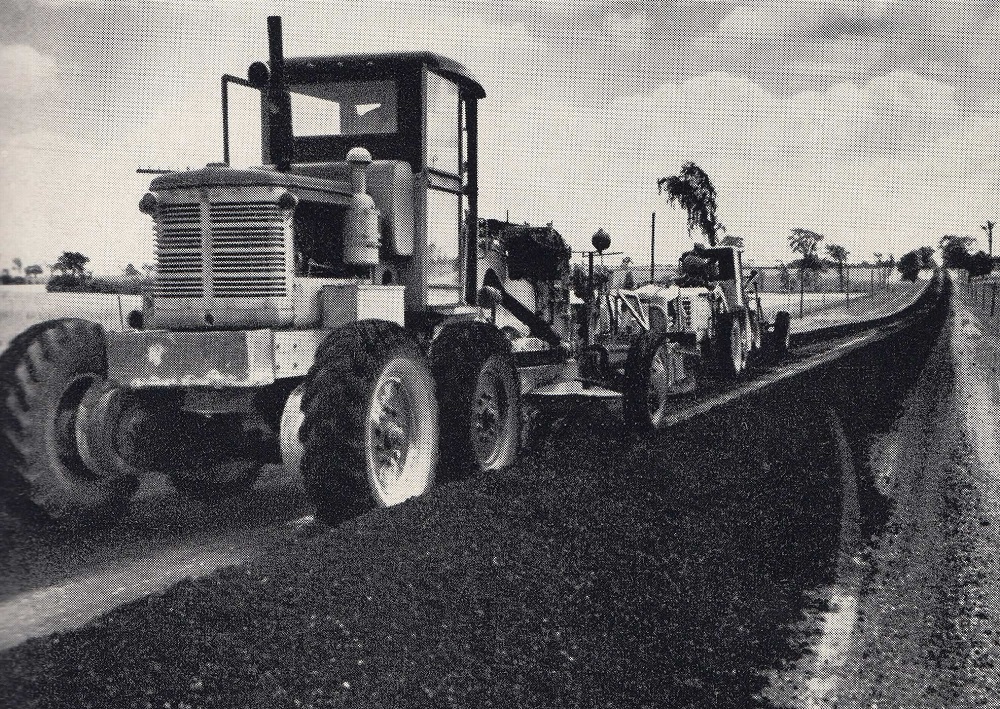 Photo en noir et blanc de machines et d’asphalte sur l’autoroute, avec des arbres à l'arrière-plan