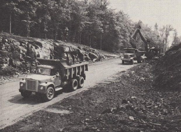 Photo en noir et blanc de camions-benne qui déplacent de la terre, avec des arbres à l'arrière-plan