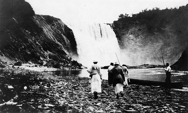 Épreuve argentique d'Elsie Reford et d'Evelyn MacInnes marchant sur les roches de la berge de la rivière Mitis, approchant du pied de la chute et sur le point d'embarquer dans leur canot pour une journée de pêche.