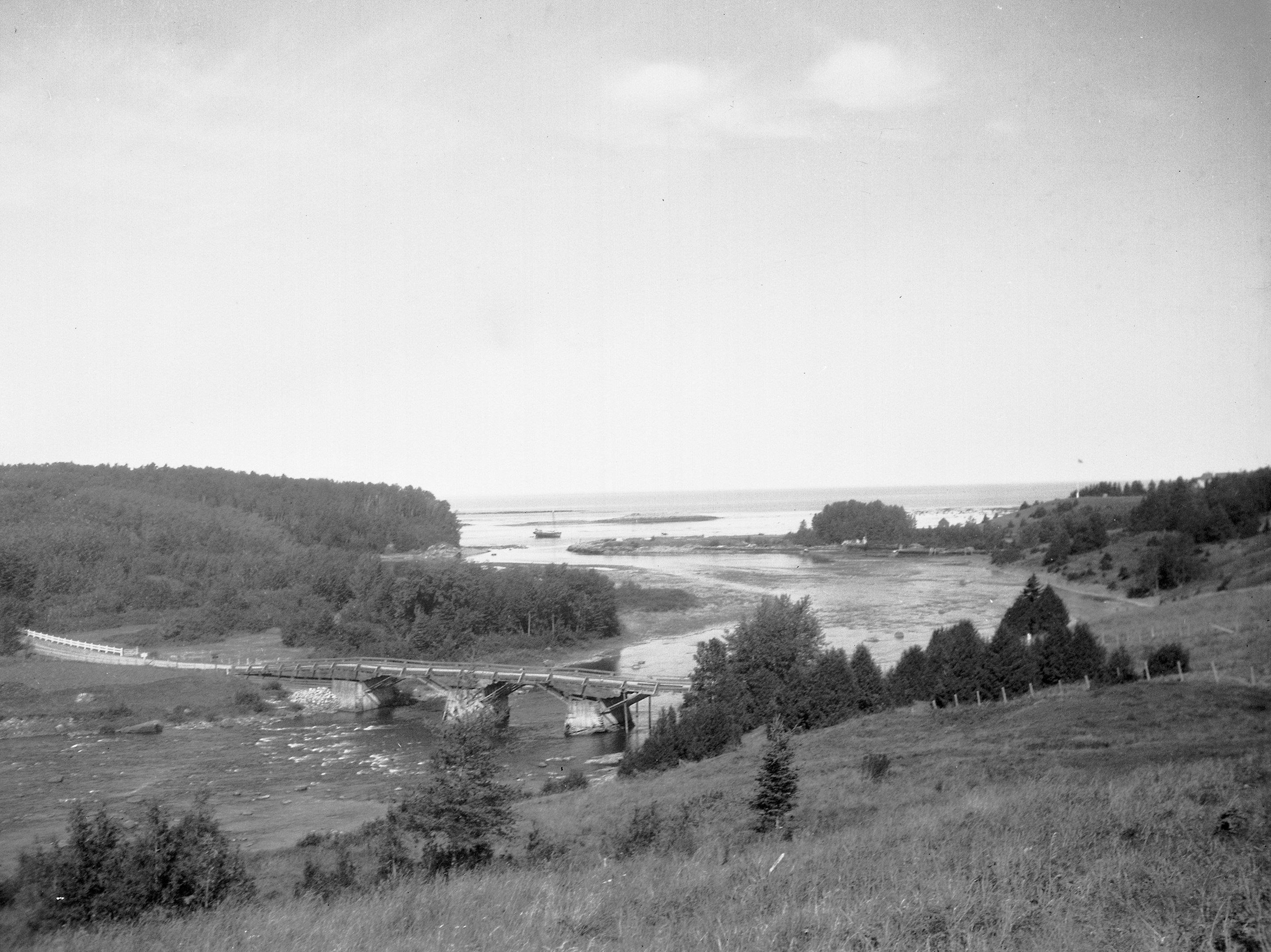 Vue de l'embouchure de la rivière Mitis sur laquelle on aperçois l'ancien pont de bois, les vestiges du quai de la Price Brothers company, une goelette et le mât du belvédère de la Villa Estevan.