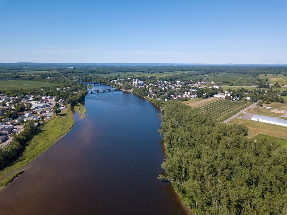 Photographie couleur de la rivière Sainte-Anne et des deux rives à la hauteur de la municipalité vue du ciel avec les deux ponts.