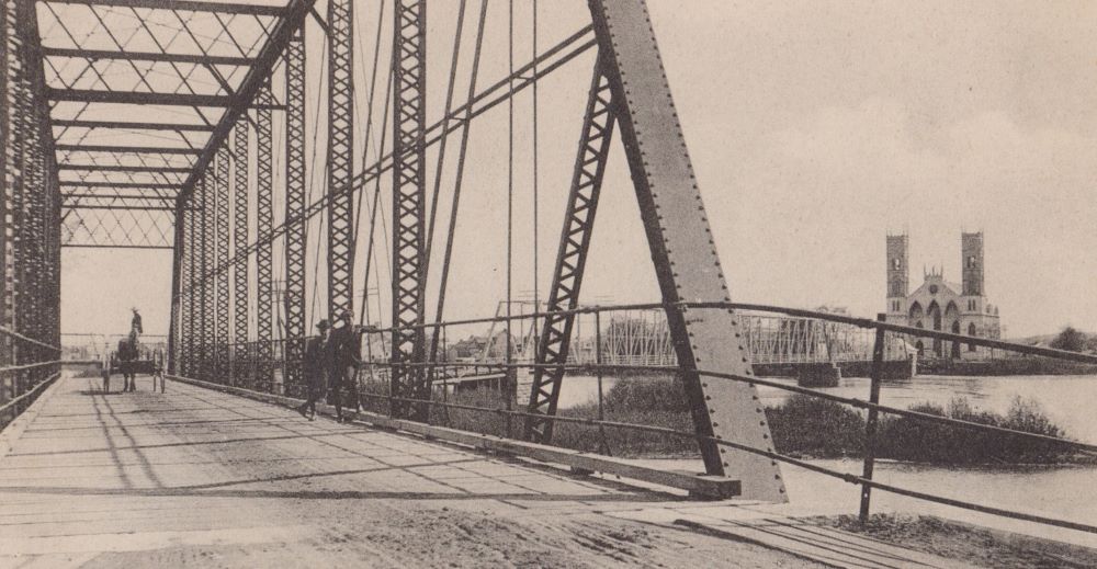Photographie en noir et blanc du pont de fer de Sainte-Anne-de-la-Pérade construit après l’éboulis de 1894 sur lequel se tiennent deux hommes et une voiture à chevaux.