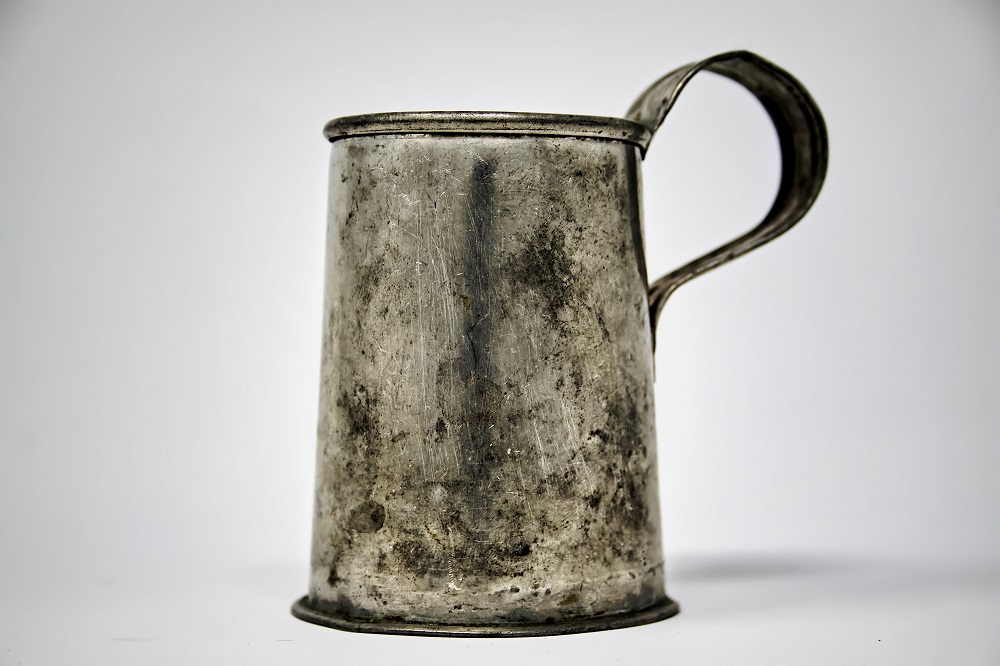 Photographie d'une tasse usée en métal et fer avec une anse.