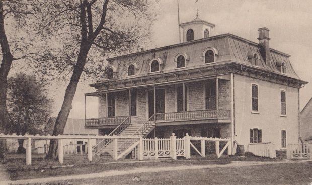 Photographie en noir et blanc du nouveau presbytère de Sainte-Anne où résidait le curé Laflèche avec toit mansardé en tôle façade en briques galerie avant et escalier central.