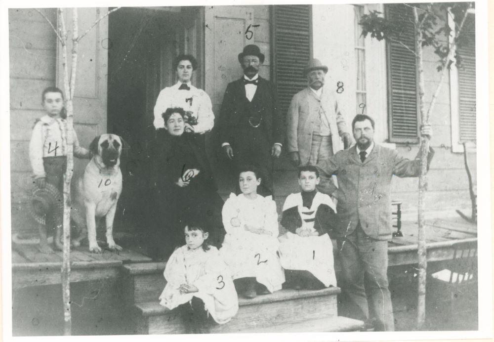 Photographie en noir et blanc de Jeffrey Alexandre Rousseau sa femme ses quatre enfants et trois autres membres de sa famille avec un chien posant devant le porche de sa maison.