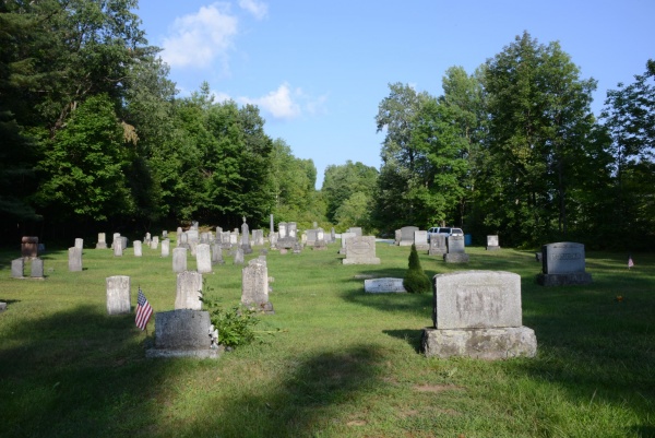 Vue d’un cimetière qui traverse la frontière, avec certaines tombes au Canada et d’autres aux États-Unis. Ici aussi, la frontière n’est pas marquée et, bien que la Commission de délimitation ait envisagé de placer sa propre borne de granit parmi les pierres tombales, elle a décidé qu’il valait mieux laisser ces âmes reposer en paix, dans le pays où elles pensaient être enterrées.