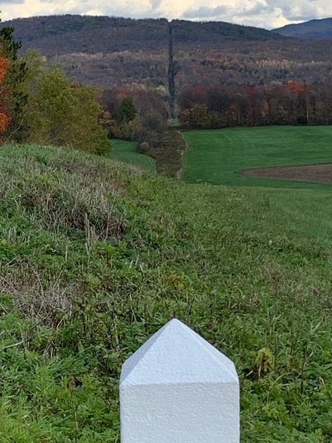 Derrière une petite borne blanche, une bande libre de végétation qui traverse champs et montagnes et marque le tracé de la frontière 