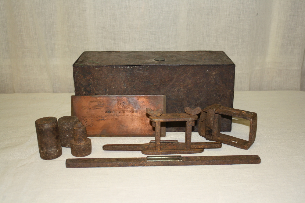 Une plaque et divers outils de faussaire disposés devant un  			   coffret en fer