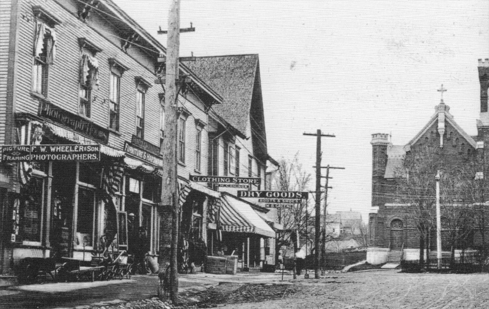 En avant-plan, on peut lire l’enseigne du studio du photographe Frank Wheeler, et tout à côté, sur une rue commerciale de Richford, des magasins de vêtements et de tissus 