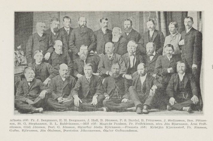 Photographie en noir et blanc d’un groupe de 30 hommes posant en trois rangées, vêtus de costumes formels du 19e siècle. Certains hommes sont assis en pose tailleur par terre au premier rang, d’autres sont assis sur des chaises au centre, et la rangée arrière est debout. La plupart portent une moustache ou une barbe, et leurs expressions sont sérieuses. Sous l’image figure une légende en islandais énumérant les noms de tous les individus sur la photo, dont Fr. J. Bergmann, St. G. Stephanson et Ólafur Guðmundsson. L’arrière-plan montre un rideau uni. 
