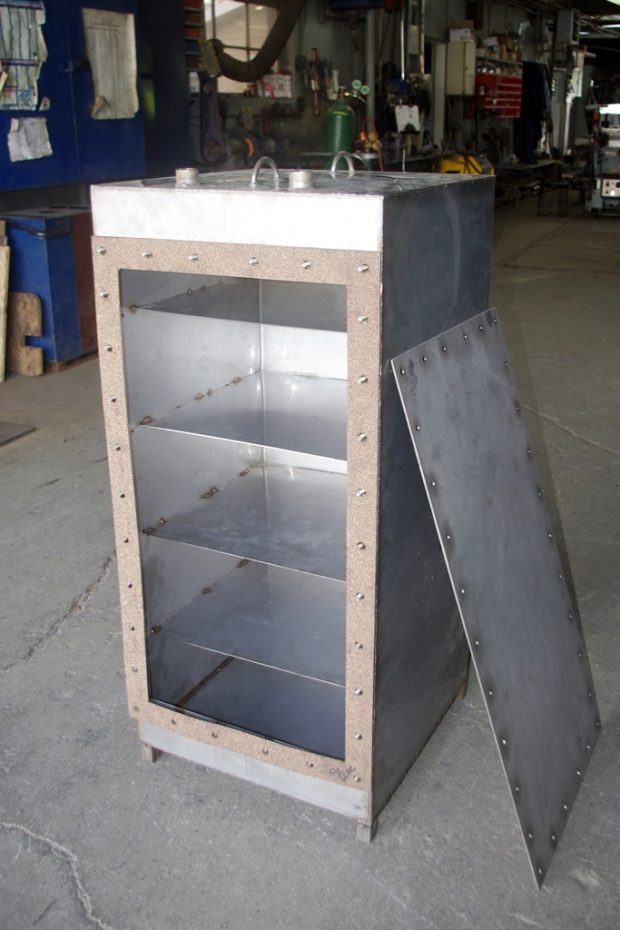 Photo couleur d’une boîte en acier dans l'atelier de fabrication Acier Lemieux. On peut voir les compartiments de la boîte ainsi que sa porte accotée à droite, de même qu’une vue partielle de l’atelier.
