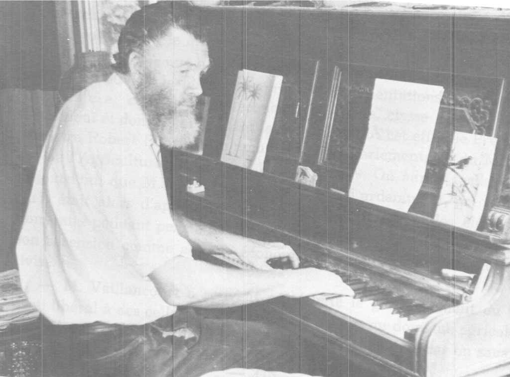 Photo noir et blanc de Dr Cecil Meade assis au piano. Des livres de partitions sont disposés sur le piano.