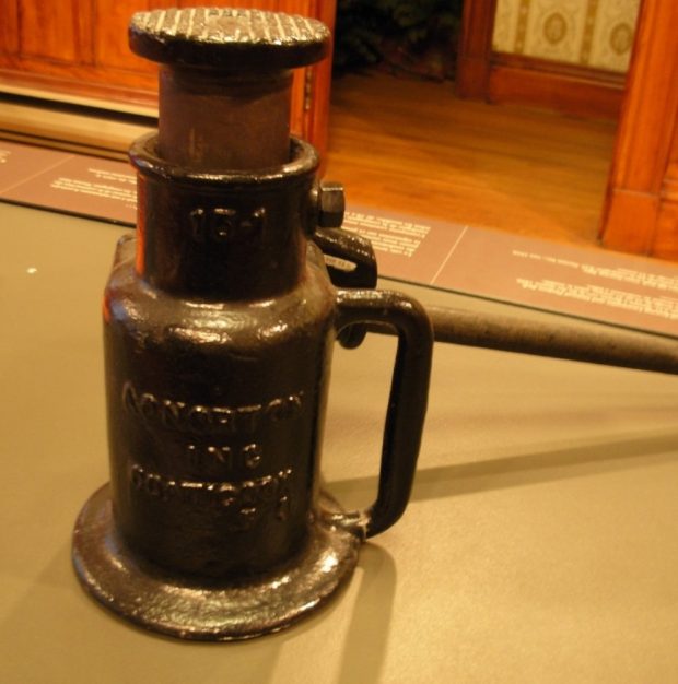 Photo couleur d’un outil de couleur noire sur un présentoir dans une salle d’exposition du Musée Beaulne. Relativement court, il porte l’inscription  « 15-1 » sur la partie supérieure et « A.O.Norton Inc. Coaticook » en dessous sur le corps. On peut voir une partie des murs de la salle et du couloir ainsi qu’une partie du plancher du couloir.