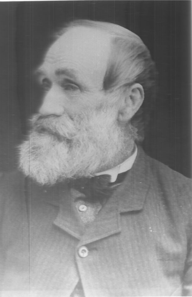 Photo noir et blanc présentant le portrait de biais de Samuel Cleveland avec une barbe et une moustache blanches, un costume gris rayé et un nœud papillon noir.