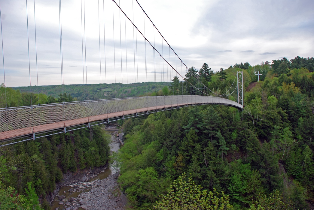Photo couleur qui montre le Pont suspendu dans un écrin de verdure et la gorge de Coaticook en contrebas.