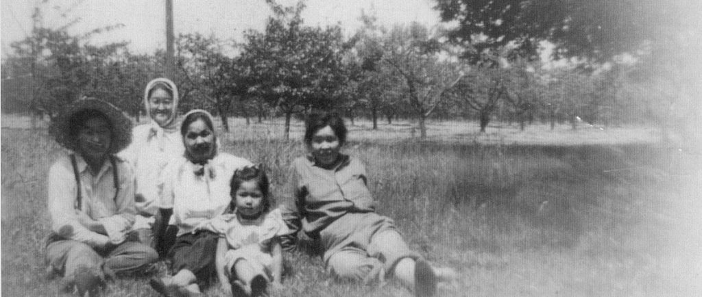 Quatre femmes et une jeune fille assises dans l’herbe d’un verger