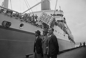  Trois hommes blancs debout observant un navire rempli de Canadiens d'origine japonaise exilés au Japon