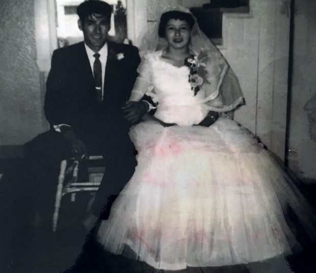 Un jeune couple assis côte à côte le jour de leur mariage. L'homme porte un complet avec cravate et la femme une robe longue en tulle et un voile sur sa tête. Photo en noir et blanc. 