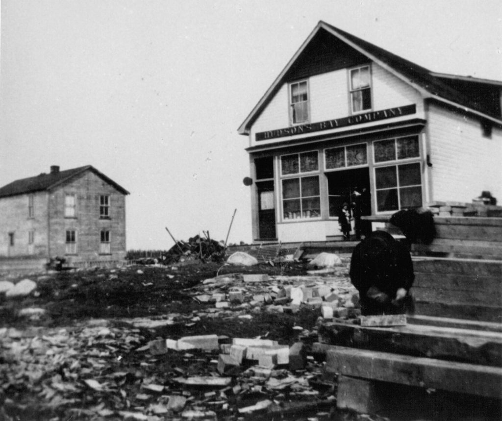 Photo noir et blanc du magasin de la Compagnie de la Baie d'Hudson à Senneterre, une petite maison blanche avec deux personnes devant. 