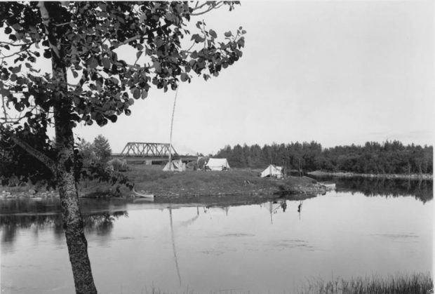 Campements autochtones sur île près de Senneterre. On y voit quelques tentes et, en arrière plan, un pont. Photo en noir et blanc. 