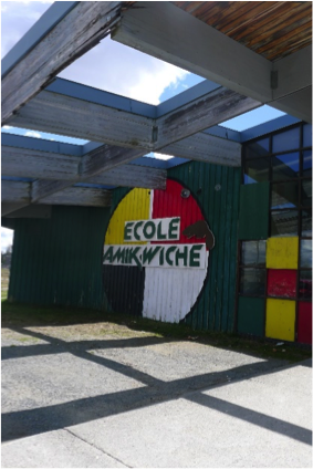 Devanture de l'école secondaire, Amik Wiche. On y voit son logo: un cercle avec quatre couleurs (rouge, jaune, blanc, noir) et un castor. Photo en couleur.