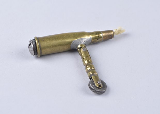 Briquet rustique et simple, fait d’une cartouche munie d’une mèche à l’extrémité. Un bras pivotant permet d’approcher la molette et la pierre de la mèche pour l’enflammer.