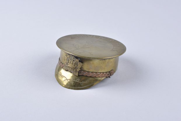 Cendrier en forme de casquette militaire avec dessus évasé, portant un insigne de laiton en forme de feuille d’érable portant le mot « Canada. »