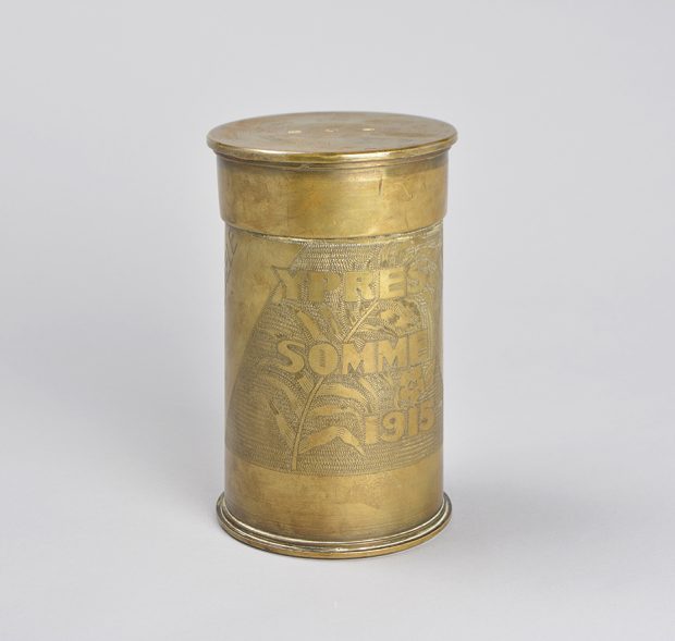 Pot à tabac fait d’une douille d’obus en laiton. Les noms « Ypres » et « Somme » ainsi que la date « 1915 » sont gravés, sur un fond comprenant une feuille de fougère et un motif ciselé.