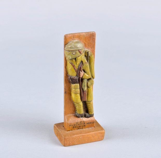 Sculpture d’un soldat en uniforme. Le bois est teint et un voile pend sous le casque, cachant le visage du soldat.