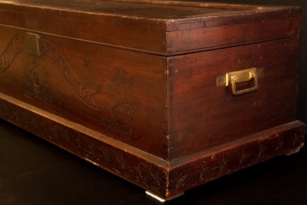Coin d’un coffre bout de lit en bois, montrant les motifs gravés et la poignée de laiton.