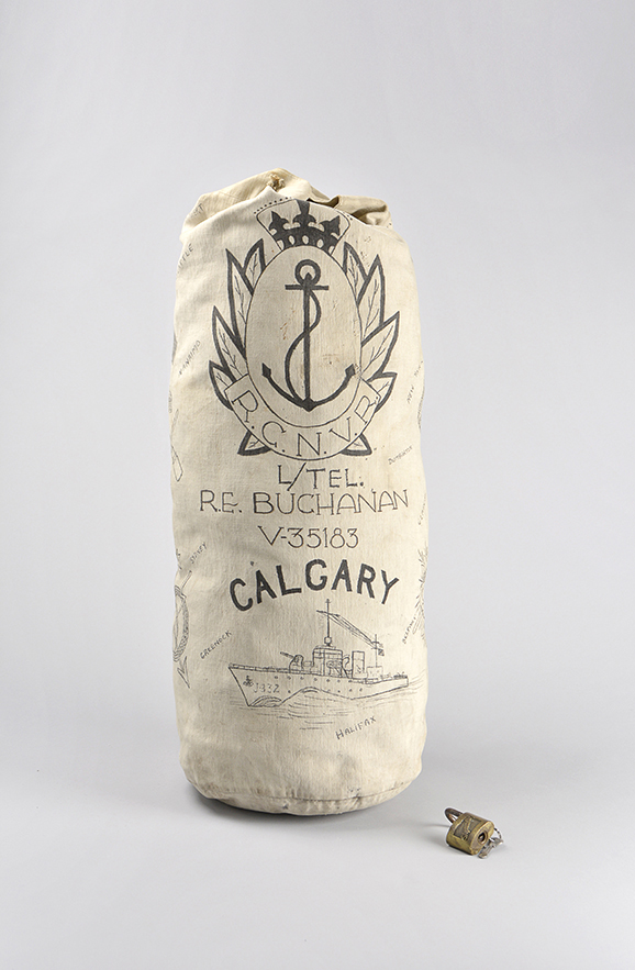 Sac de paquetage marin de couleur crème, avec le logo de la Réserve de volontaires de la Marine royale du Canada, au-dessus du nom d’un marin et de l’image d’un navire en mer. 