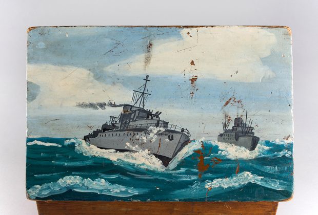 Image en gros plan du couvercle du nécessaire de marin, montrant deux vaisseaux de guerre sur une mer agitée. 