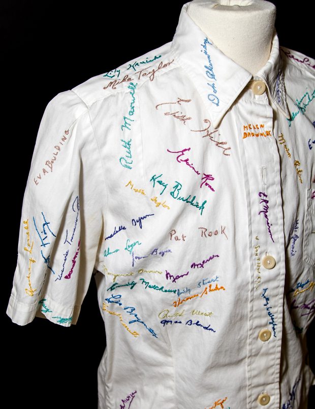 Devant d’une chemise à collet blanc, portant des signatures brodées en fil de diverses couleurs.