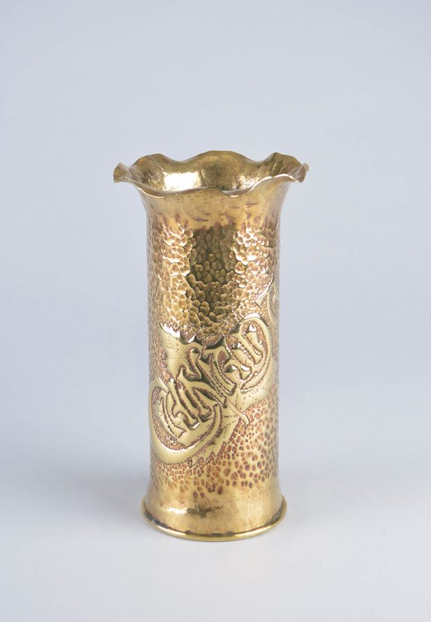 Grand vase en laiton, décoré de motifs côtelés à la partie inférieure et d’une ouverture ondulée. Le milieu est couvert de bosselures et le mot « Canada » est gravé  selon un angle ascendant.