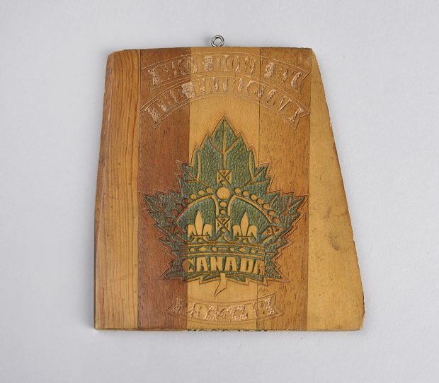 Plaque gravée sur un bout d’hélice d’avion. La surface en bois fini  porte une feuille d’érable verte, avec une couronne et le mot « Canada » au centre.  