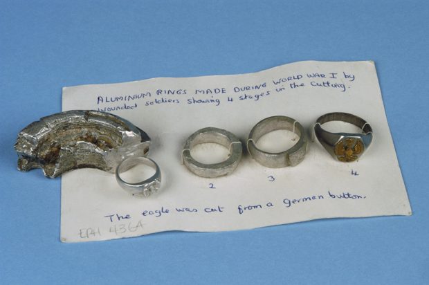 Quatre anneaux d’aluminium à diverses étapes consécutives de leur fabrication. Ils sont fixés sur une carte avec des explications écrites à la main. 