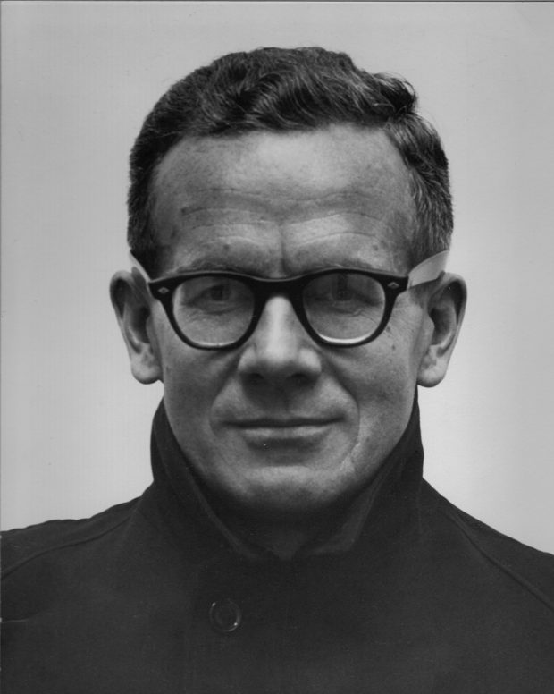 Photo professionnelle en noir et blanc d’un homme d’une quarantaine d’années, portant des lunettes à monture noire, regardant fixement l’appareil photo avec un léger sourire.